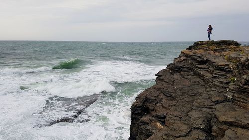  woman stands holding a baby  on cliff by the sea against sky