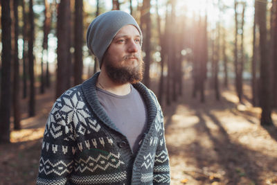 Hipster looking away while standing against trees in forest