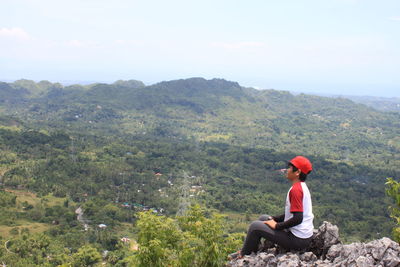 Man sitting on mountain against sky