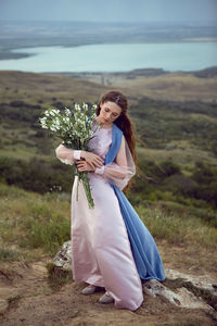 Woman stands on a mountain cliff in a blue long dress in summer
