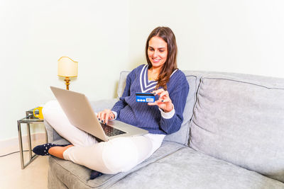 Young woman using phone while sitting on laptop