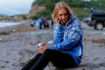 Young woman talking on mobile phone while sitting at beach