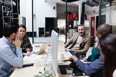 Business colleagues discussing in meeting while using technologies at creative office