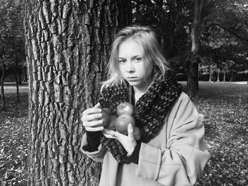 Portrait of young woman with apple standing by tree trunk at park