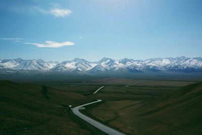 Road on landscape leading towards snow covered mountains against sky