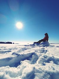 Man sitting on snow against sky