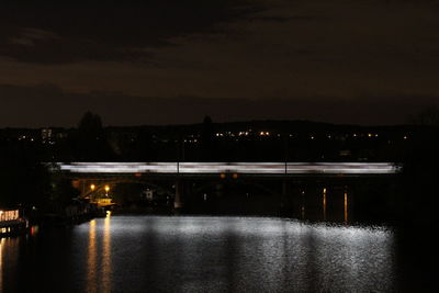 Illuminated bridge over river against sky at night