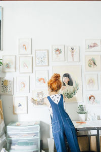 Rear view of female artist hanging paintings on wall in studio