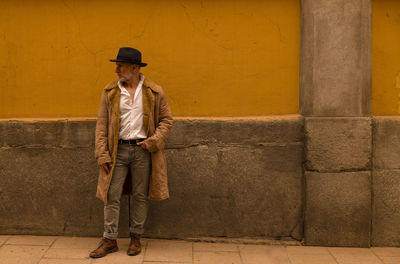 Adult man in hat and coat against yellow wall on street. madrid, spain