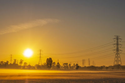 Electric pole and electric cable on the field in the countryside with sunrise sky.