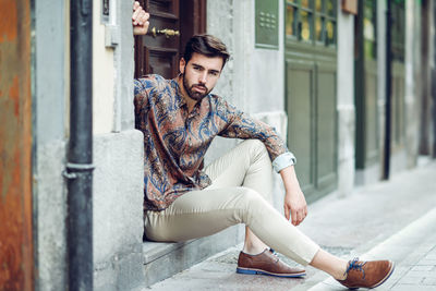 Portrait of young man sitting at entrance door