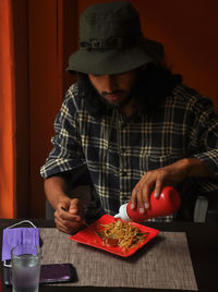 A bearded and long haired young man eating noodles in the restaurant during covid-19 pandemic. 