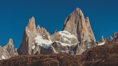 Low angle view of snowcapped mountains against clear blue sky