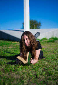 Young woman reading book on field against sky