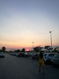 Rear view of woman standing on road against sky during sunset