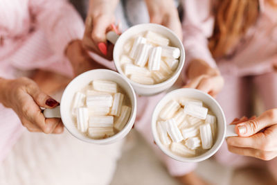 A group of girls in pajamas hold drinks coffee mugs with marshmallows in a cozy room at home