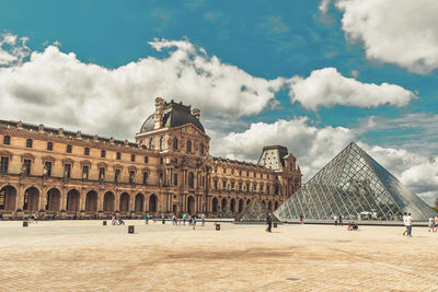 Group of people in front of historical building against cloudy sky