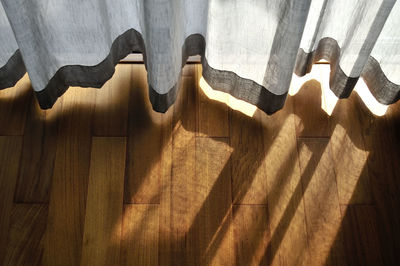 High angle view of sunlight through curtain on hardwood floor at home