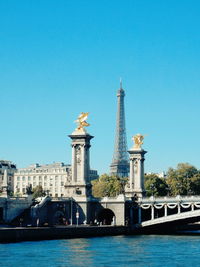 Eiffel tower by pont alexandre iii and seine river against clear blue sky in city