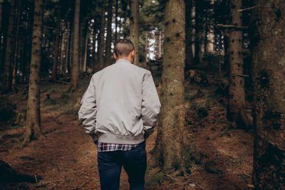 Rear view of man standing amidst trees in forest