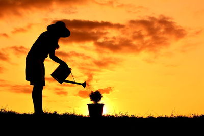 Silhouette of woman watering pot plant at sunset