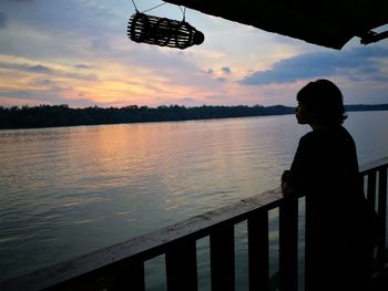 Man standing by river against sky during sunset