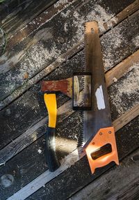 High angle view of hand saw and axe with mobile phone on deck