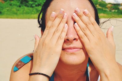 Close-up of woman with hands covering eyes at beach on sunny day