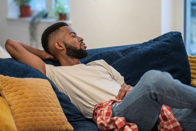 Side view of young man sitting on sofa at home