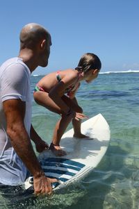 Instructor teaching girl to surf in sea
