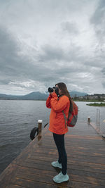 Rear view of woman photographing while standing at beach against sky