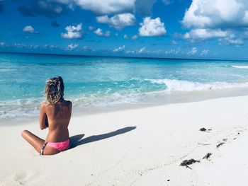 Rear view of woman sitting on beach against sky