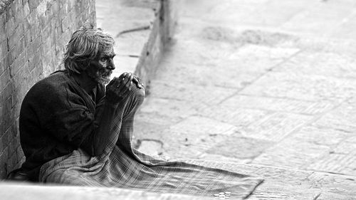 Old man sitting at sidewalk against wall