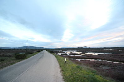 Road passing through landscape against cloudy sky
