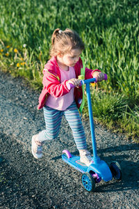 Cute girl riding push scooter on road