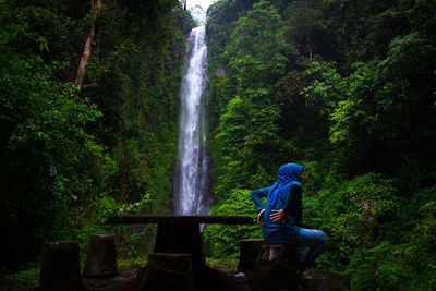 Side view of man sitting on rock in forest