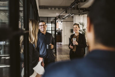 Businessmen and businesswomen discussing while standing at corridor in office