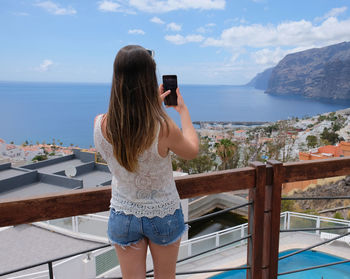 Rear view of woman photographing sea against sky