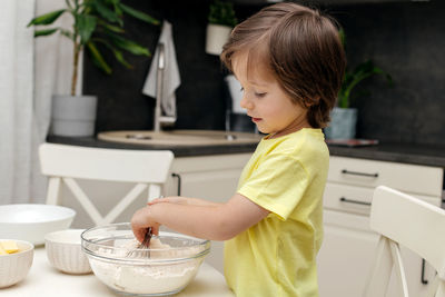 The boy prepares dough for biscuit or baking in the kitchen. the kid mixes the ingredients