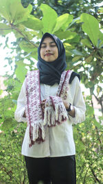 Smiling young woman with eyes closed standing against trees