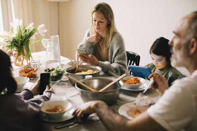 Family using gadgets while sitting at dining table