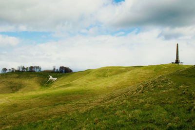 Scenic view of grassy hill against cloudy sky