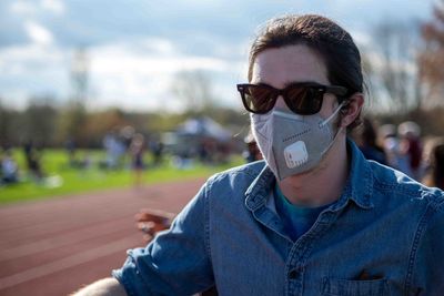 Young man with face mask stands by athletic track