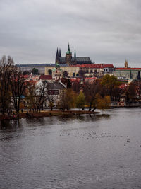 View of buildings by river against cloudy sky