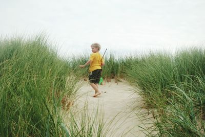 Full length of boy amidst grass at beach against sky