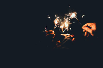 Close-up of friends holding illuminated sparklers at night