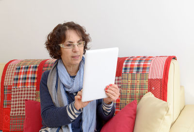 Mature woman using digital tablet while sitting on sofa at home