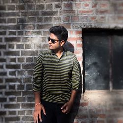 Young man wearing sunglasses standing by brick wall