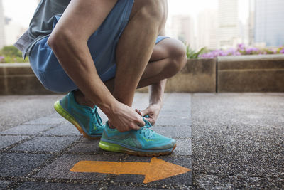 Low section of man tying shoe lace while kneeling by arrow symbol on floor