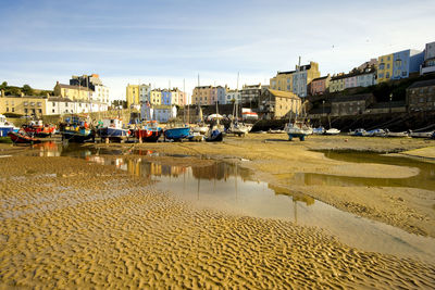 Boats moored on beach by buildings against sky